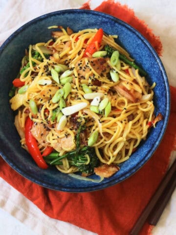 A bowl of Vegan Sweet Chilli Chicken Noodles on a red napkin with wooden chopsticks