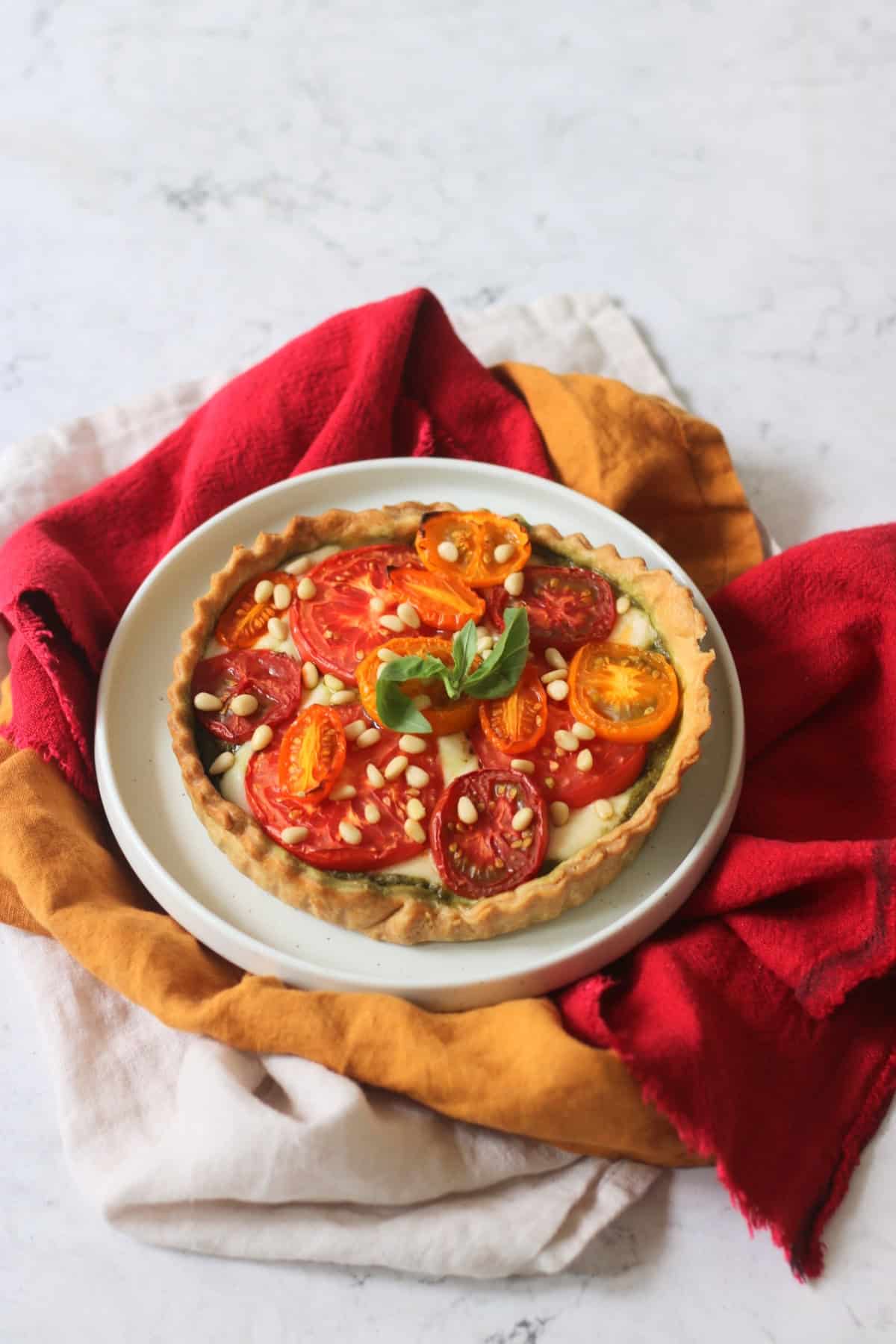 Vegan Tomato Mozzarella and Pesto Picnic Tart served on a white plate with red and yellow napkins