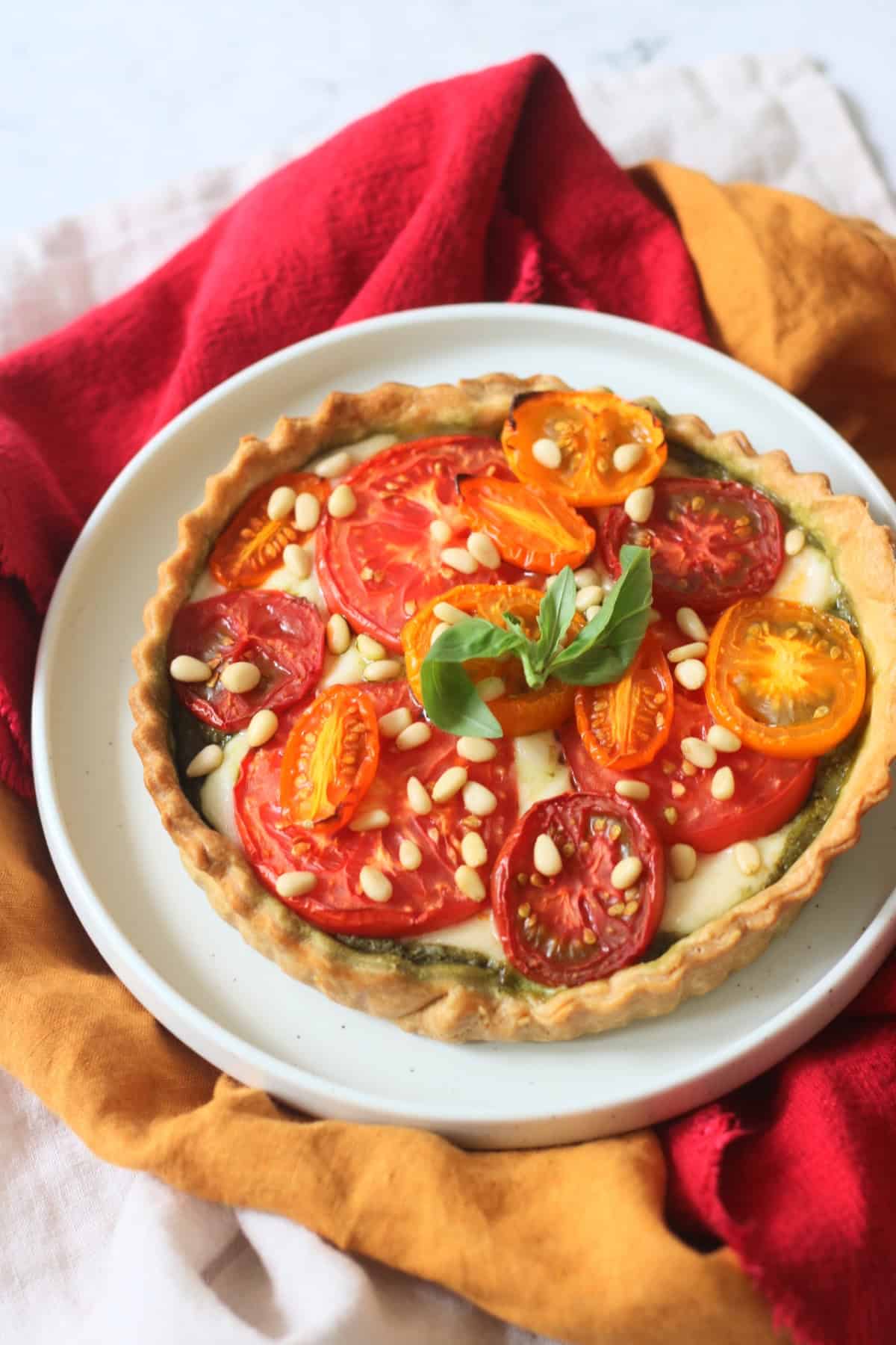 Vegan Tomato Mozzarella and Pesto Picnic Tart served on a white plate with red and yellow napkins