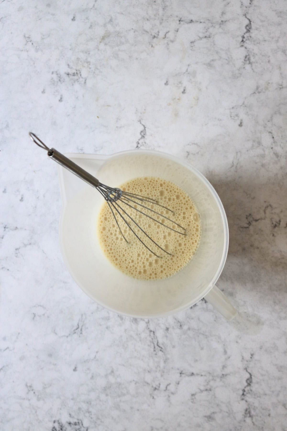 Whisking plant milk, vanilla and apple cider vinegar in a plastic jug