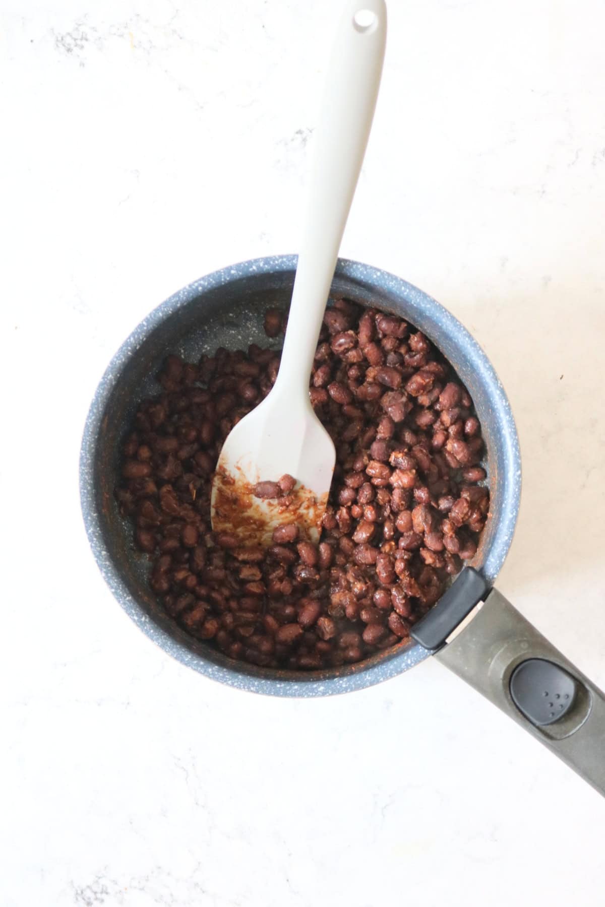 Black beans being heated in a saucepan with Cajun spices, stirred by a grey spatula