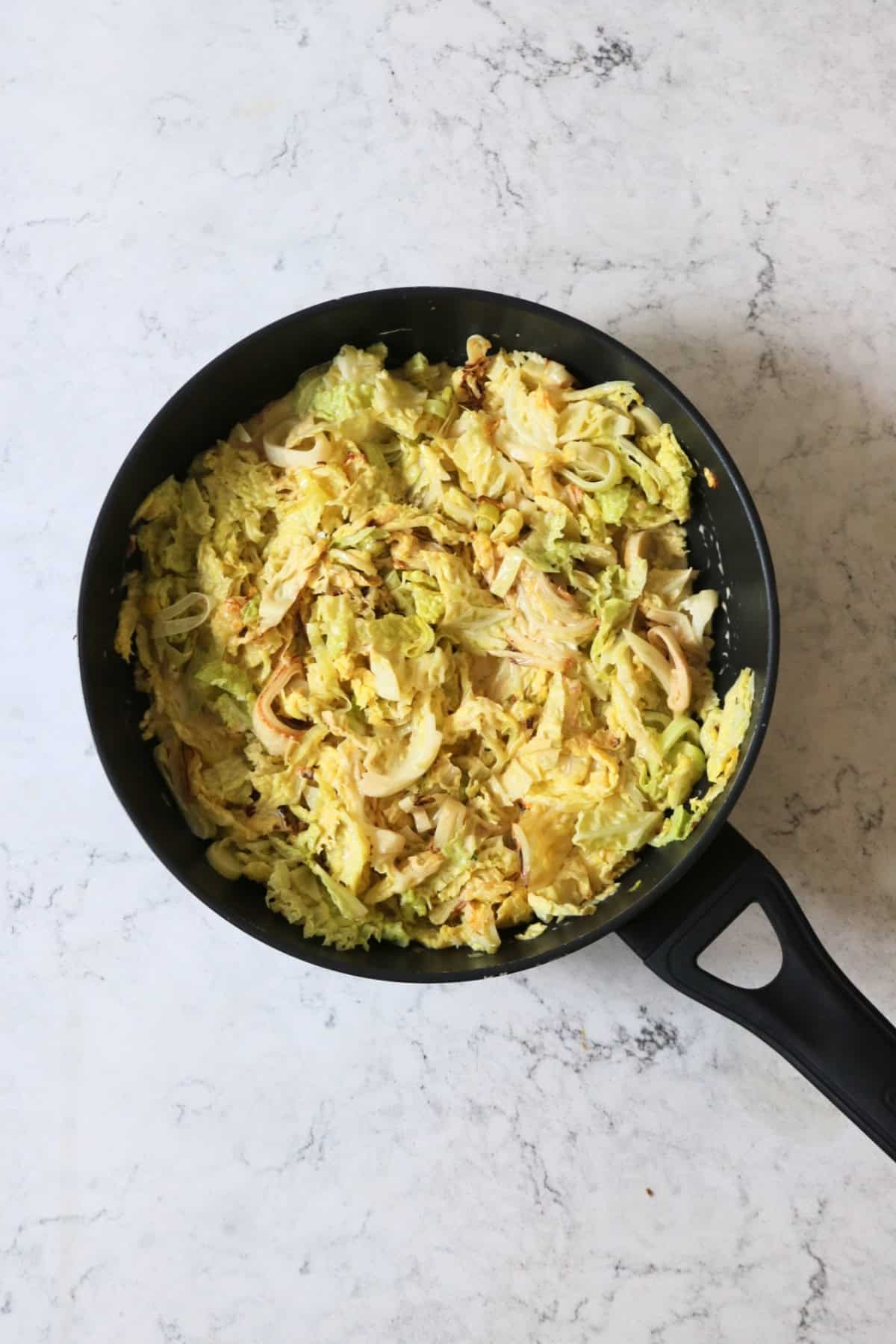 Vegan creamed cabbage and leeks cooking in a large flat bottomed frying pan