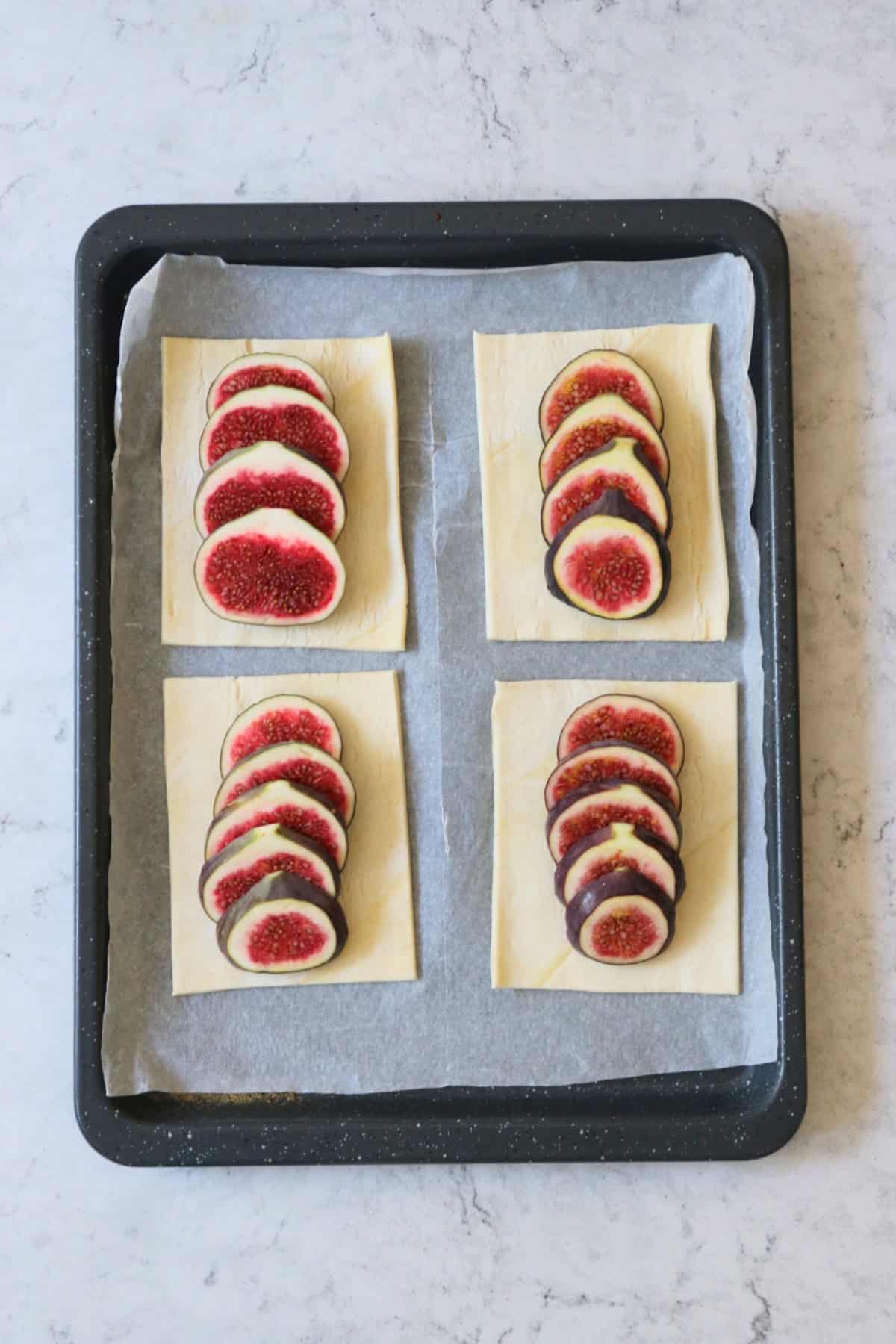 Four rectangles of unbaked puff pastry, each with a fig sliced and fanned out on top