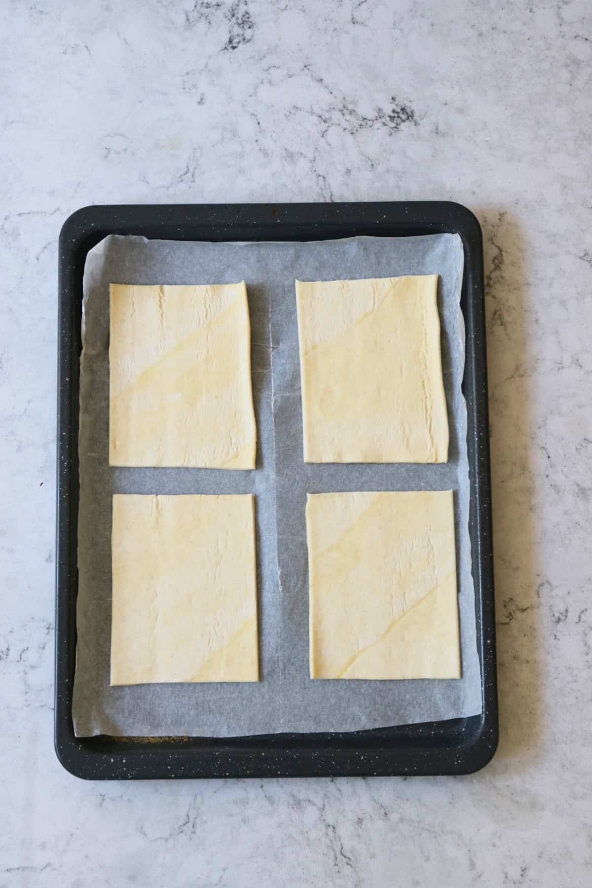 Four rectangles of unbaked puff pastry on a baking tray lined with baking paper