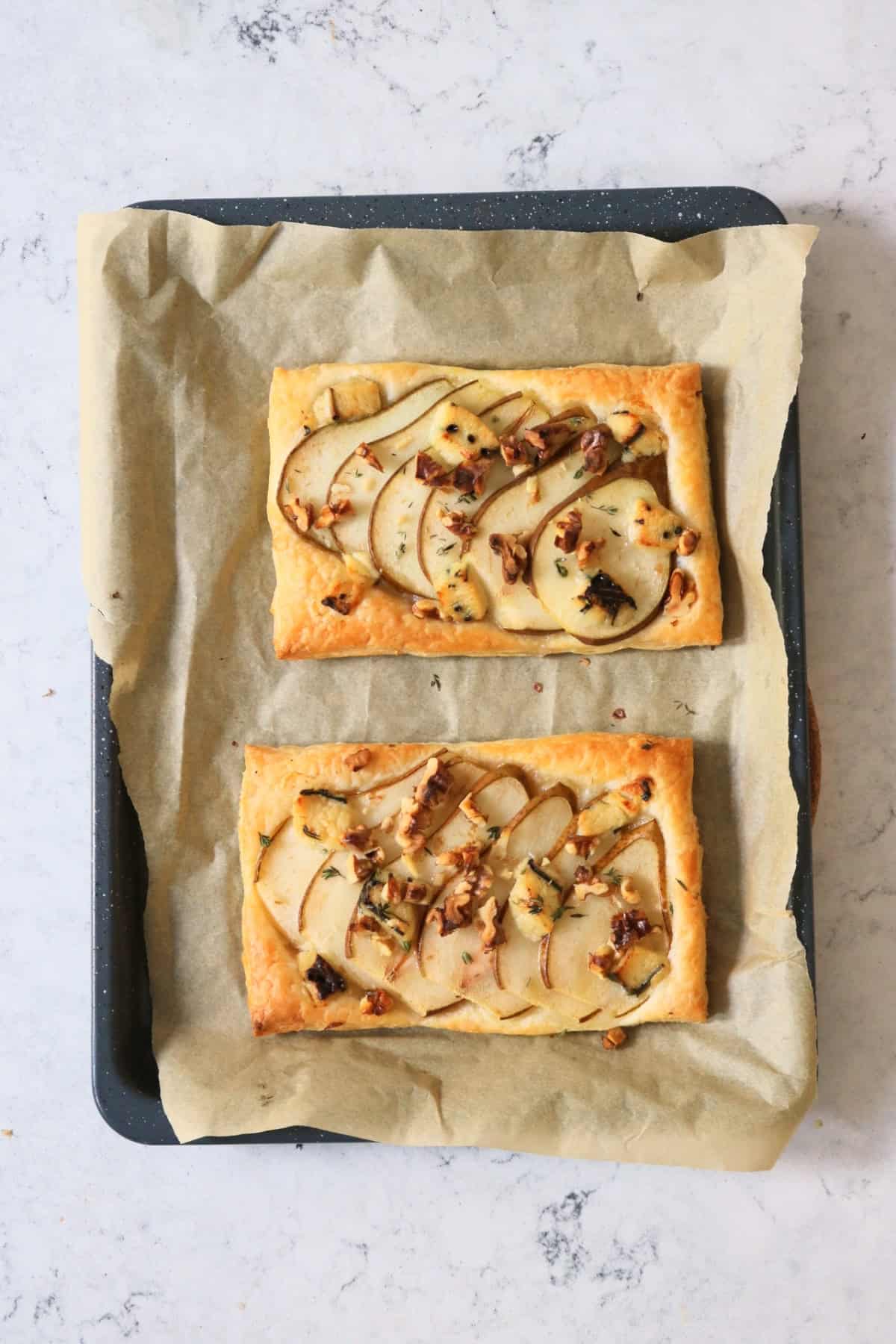Two freshly baked Vegan Pear and Blue Cheese Tarts on a baking sheet fresh out of the oven