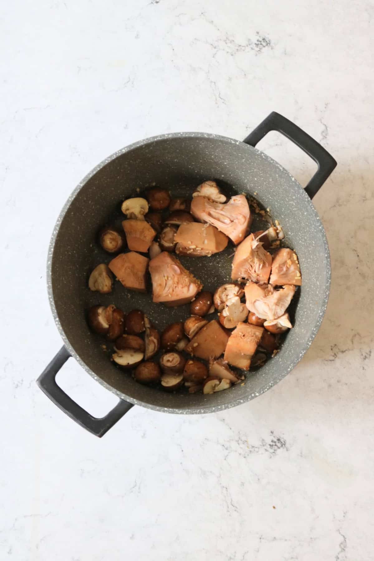 Frying jackfruit and chestnut mushrooms with garlic in a large stewing pot
