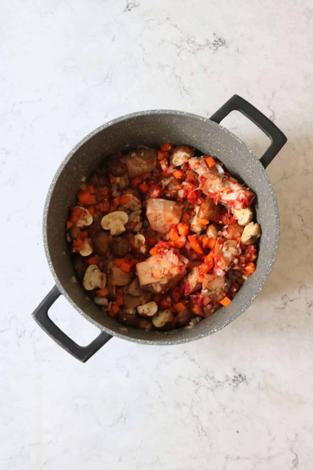 Frying the base ingredients of Vegan Coq Au Vin in a large stewing pot before adding stock