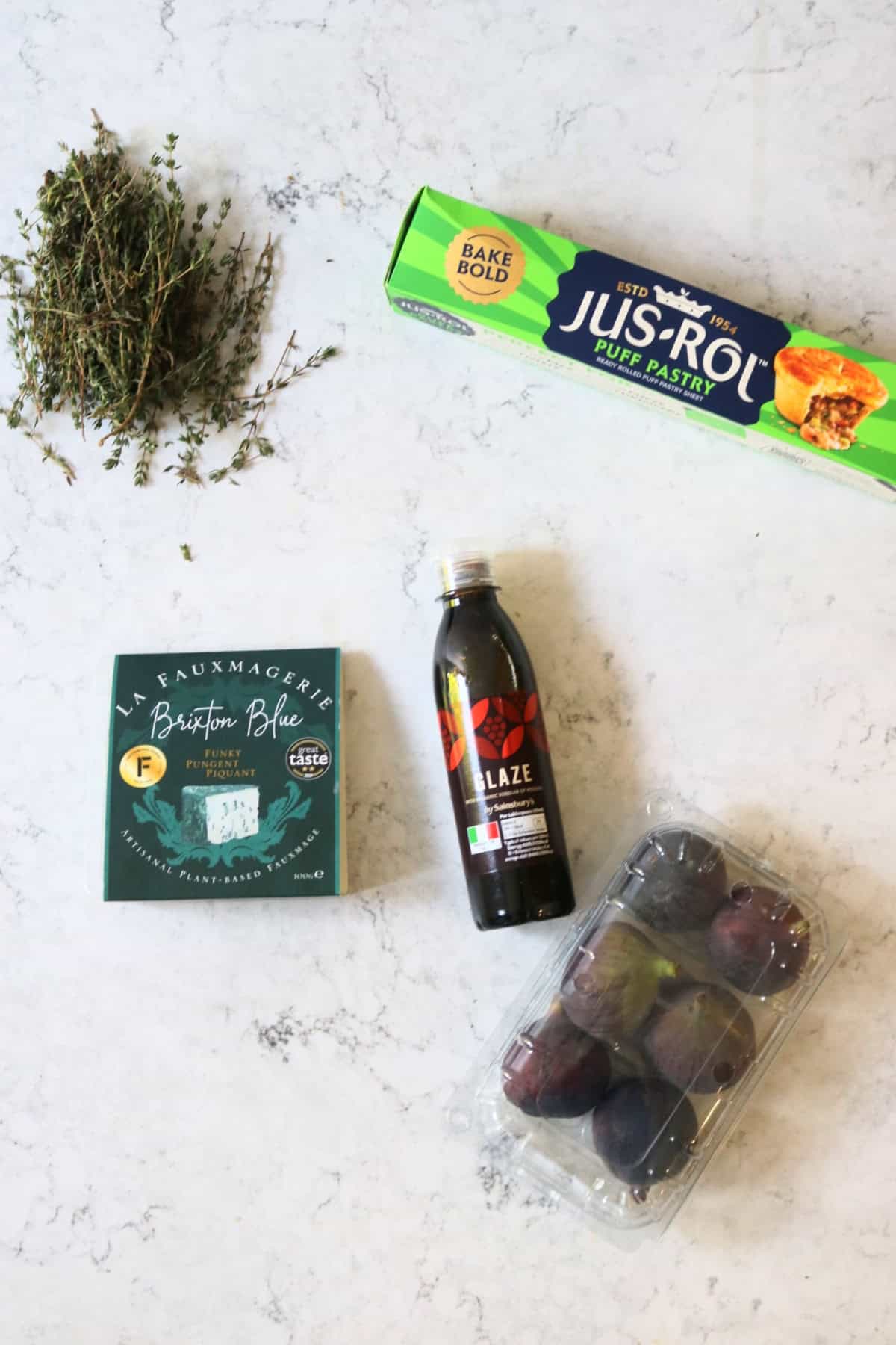 Fresh thyme, ready rolled puff pastry, vegan blue cheese, balsamic glaze and a pack of figs laid out on a white marble counter top