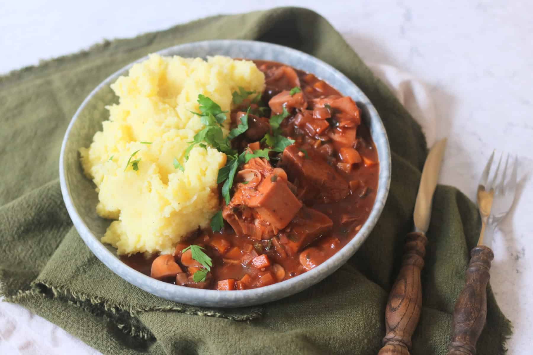 A plate of Vegan Coq Au Vin served alongside fluffy mashed potatoes