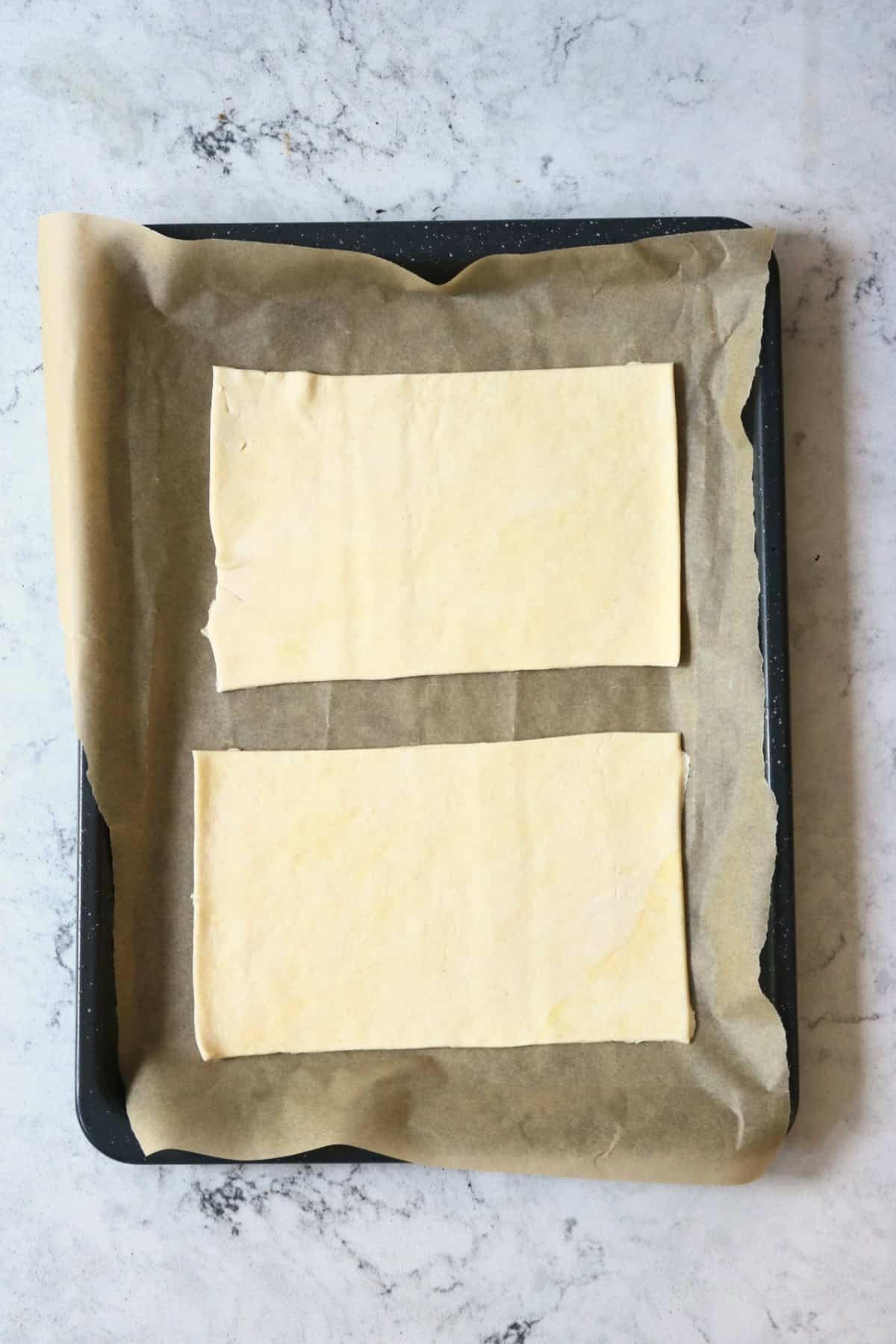 Two rectangles of unbaked puff pastry on a baking sheet