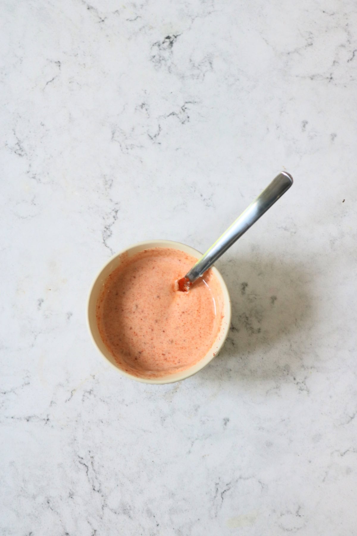 A smoky yogurt dressing in a small mixing bowl being stirred with a metal spoon