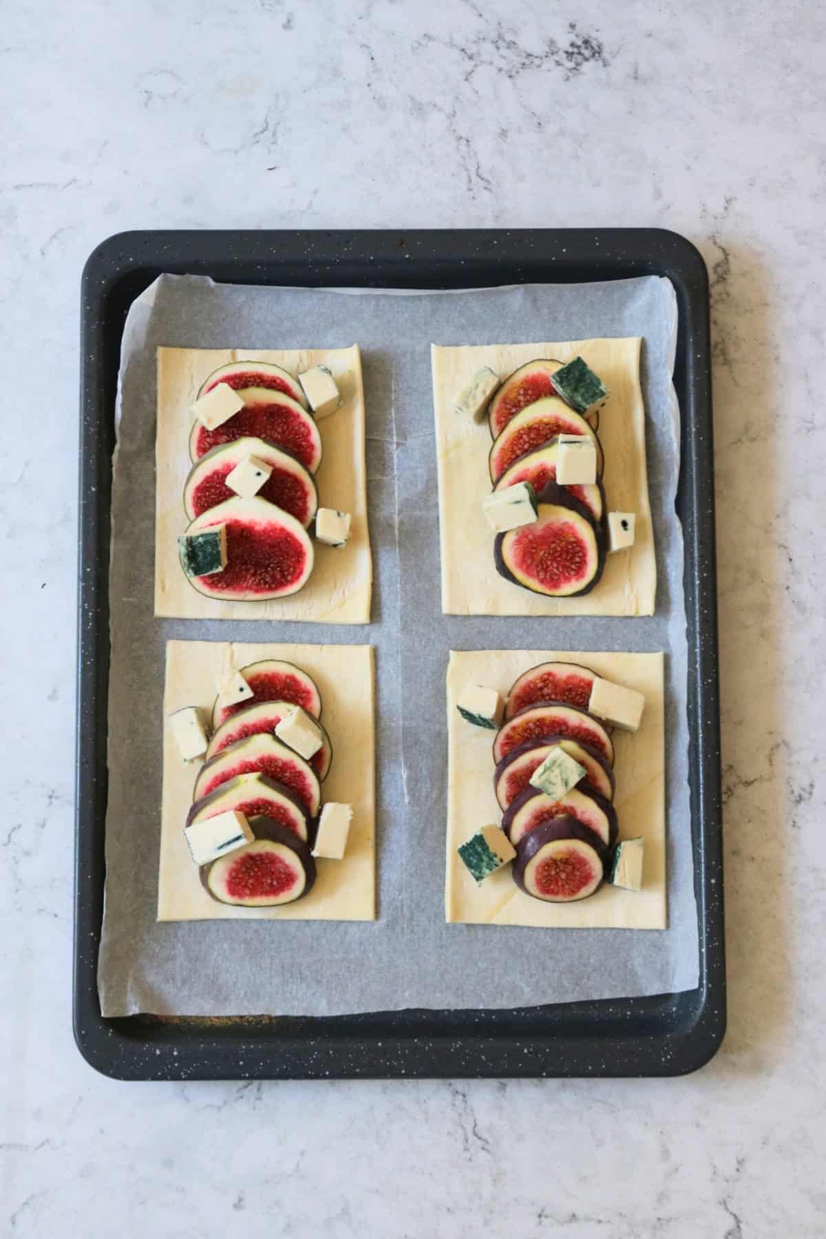 Four rectangles of unbaked puff pastry, each with a fig sliced and fanned out on top and vegan blue cheese scattered on top