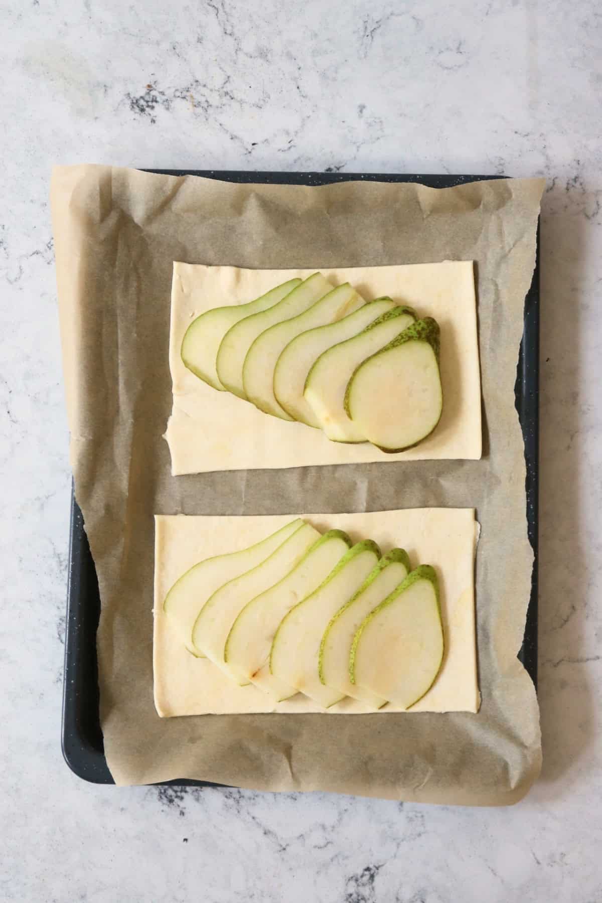 Two rectangles of vegan puff pastry laid on a baking sheet and topped with slices of pear