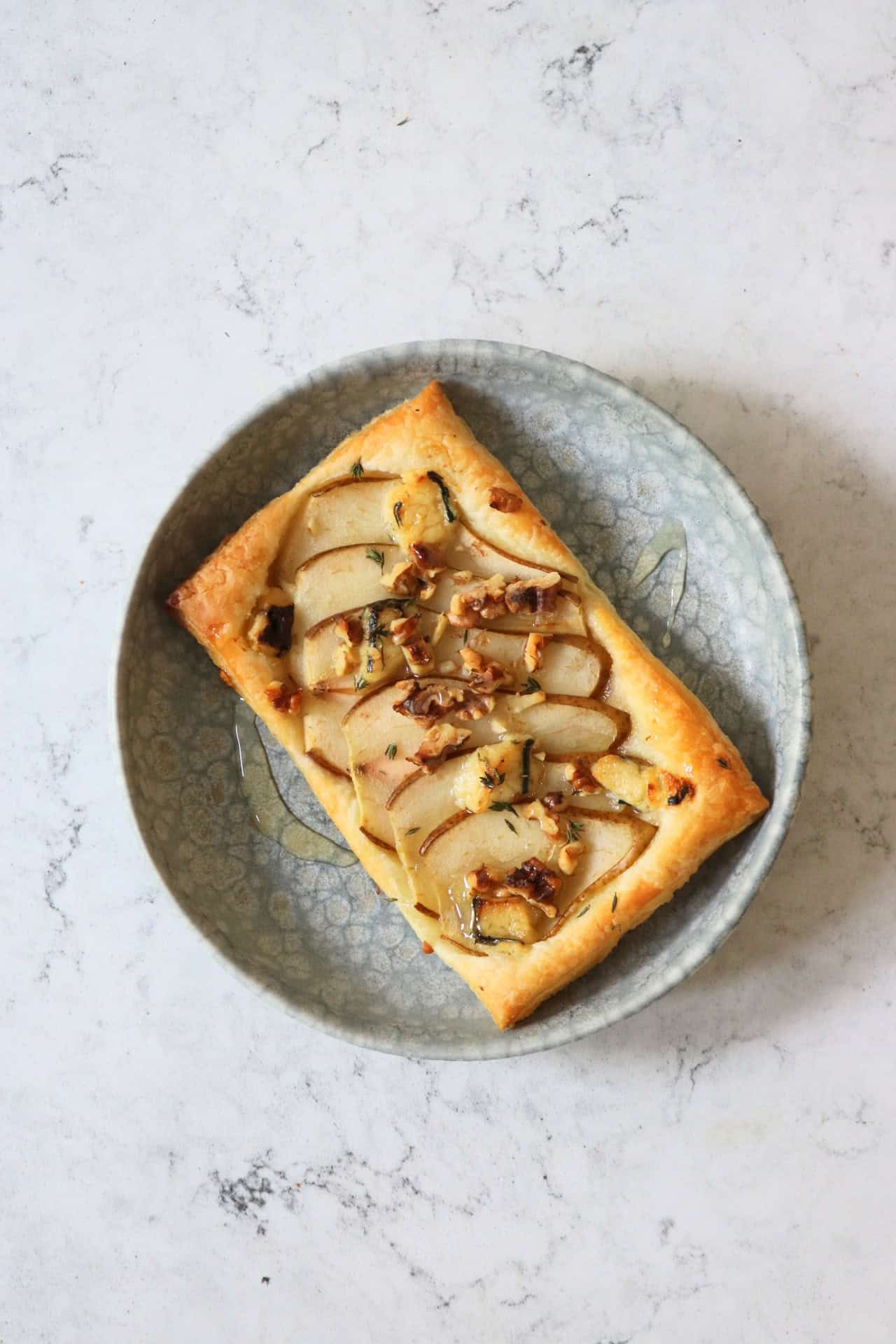 A single Vegan Pear and Blue Cheese Tart drizzled with vegan honey on a plate