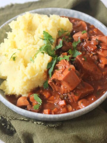 A plate of Vegan Coq Au Vin served alongside fluffy mashed potatoes