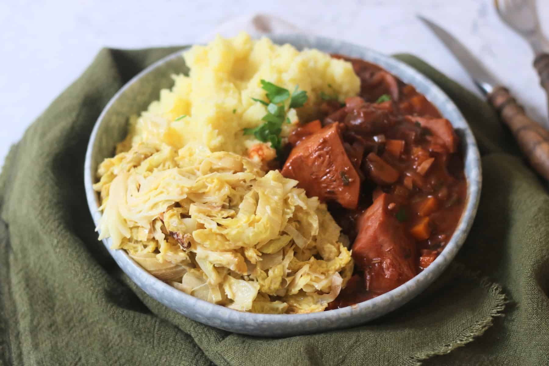 A side of Vegan Creamed Cabbage and Leeks served on a plate with vegan coq au vin and mashed potatoes