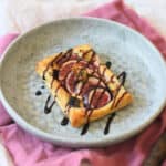 A Vegan Fig and Blue Cheese Tart on a blue plate, drizzled with balsamic glaze and served with a pink napkin