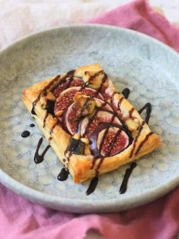 A Vegan Fig and Blue Cheese Tart on a blue plate, drizzled with balsamic glaze and served with a pink napkin