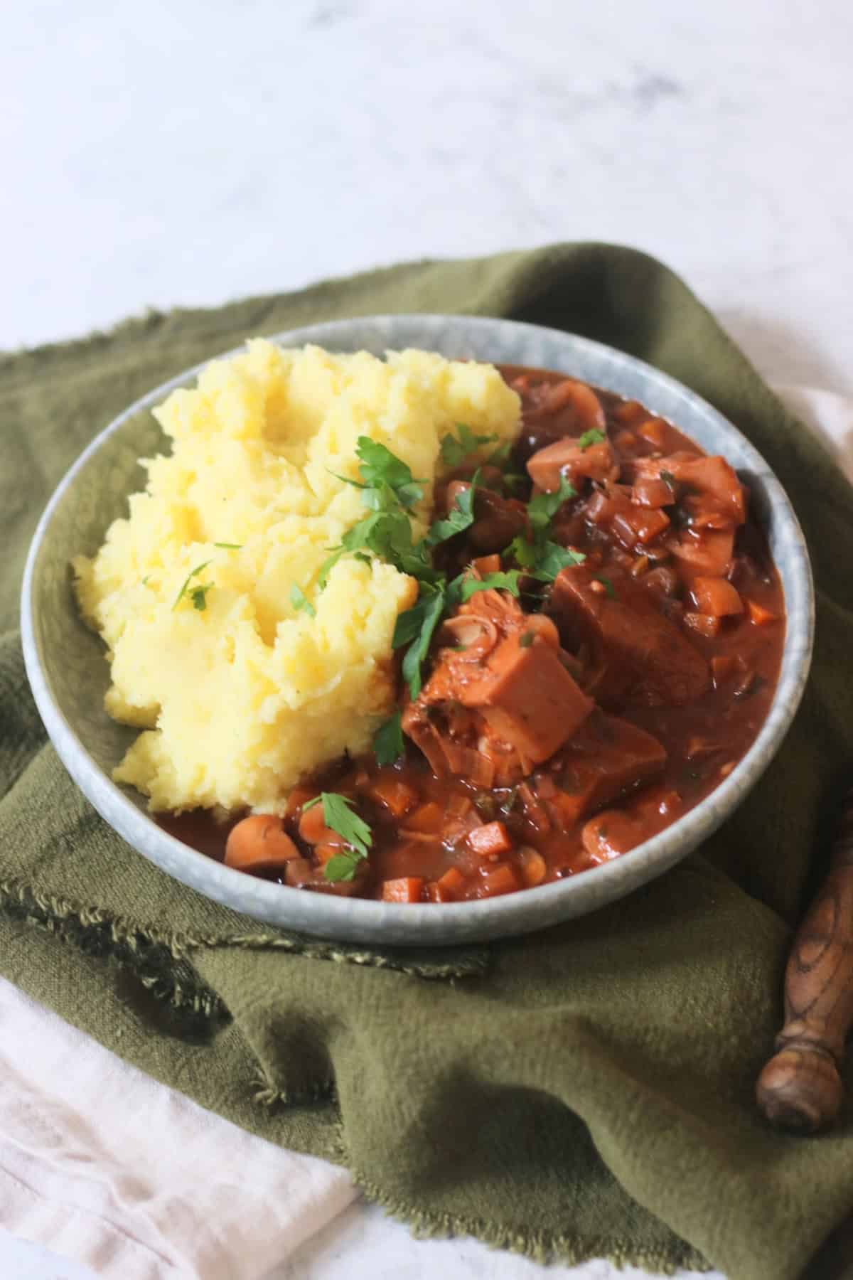A plate of Vegan Coq Au Vin served alongside fluffy mashed potatoes