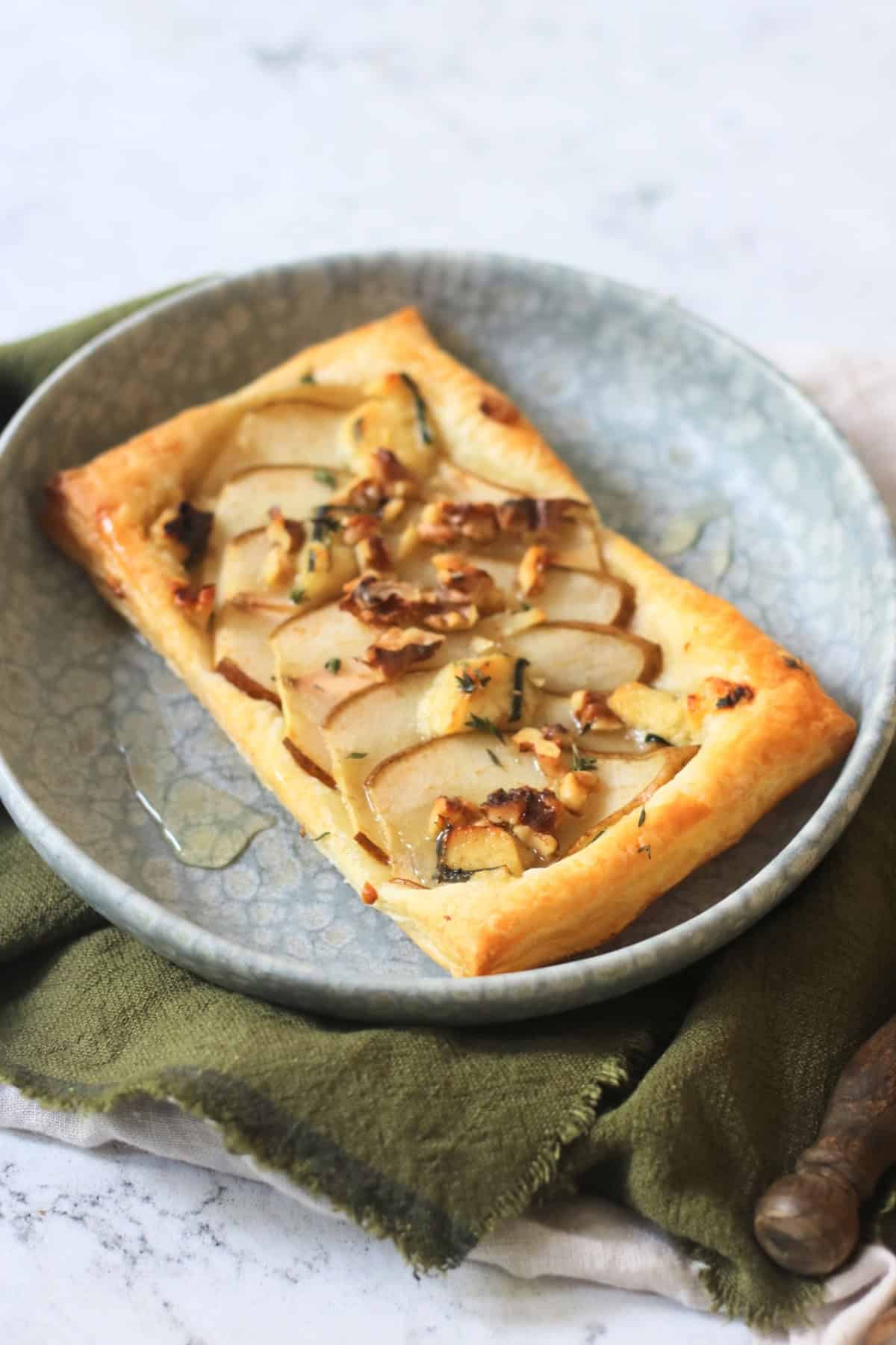 A Vegan pear and blue cheese puff pastry tart topped with walnuts, fresh thyme and vegan honey served alongside a green napkin