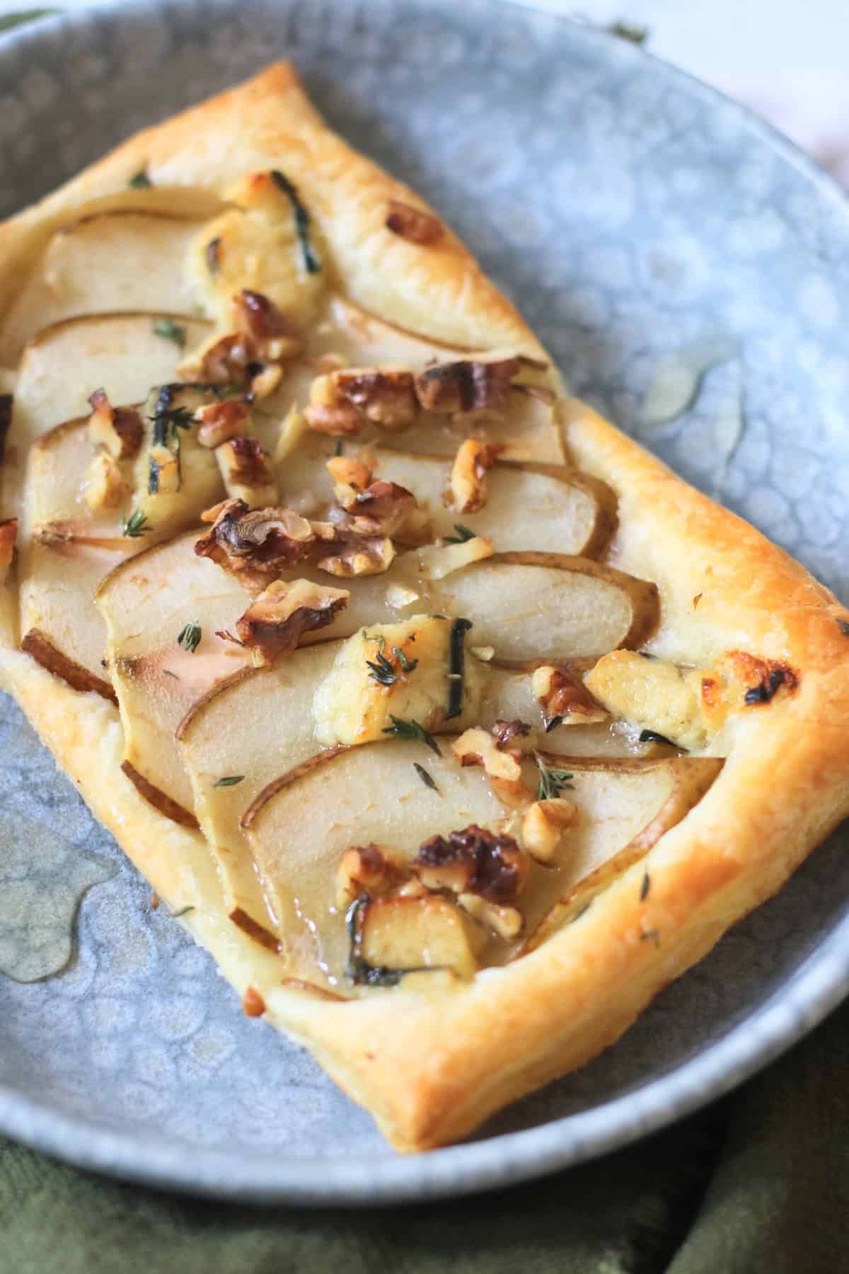 A Vegan pear and blue cheese puff pastry tart topped with walnuts, fresh thyme and vegan honey served alongside a green napkin